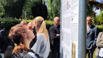 Eine junge Frau steht vor der Tafel und liest den Inhalt. Im Hintergrund weitere Besucher.